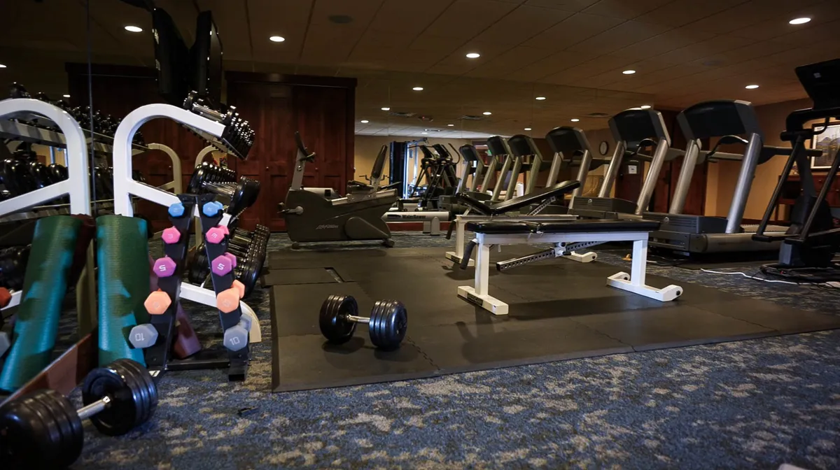 A well-equipped fitness center featuring treadmills, exercise bikes, dumbbells, and a weight bench. The space is bright and energetic, inviting guests to maintain wellness routines during their stay.