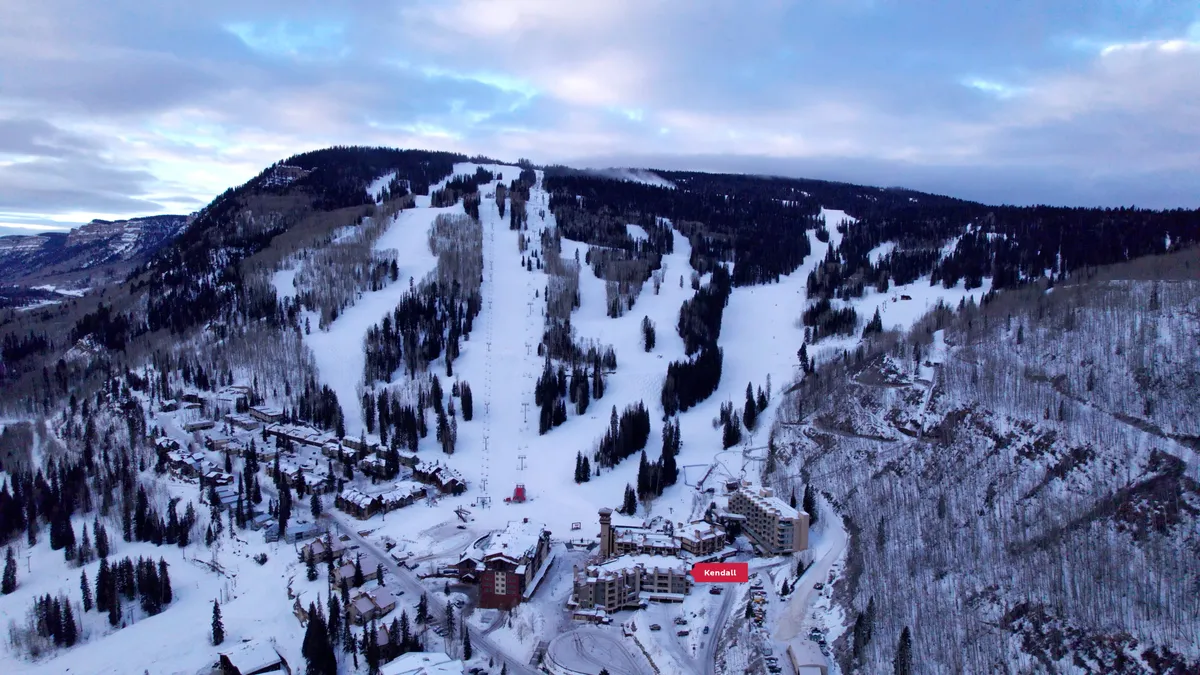 A sweeping view of snow-capped mountain ranges with ski slopes, resort buildings nestled at their base, and a vibrant sky at sunset, evoking the tranquility and grandeur of the alpine setting.